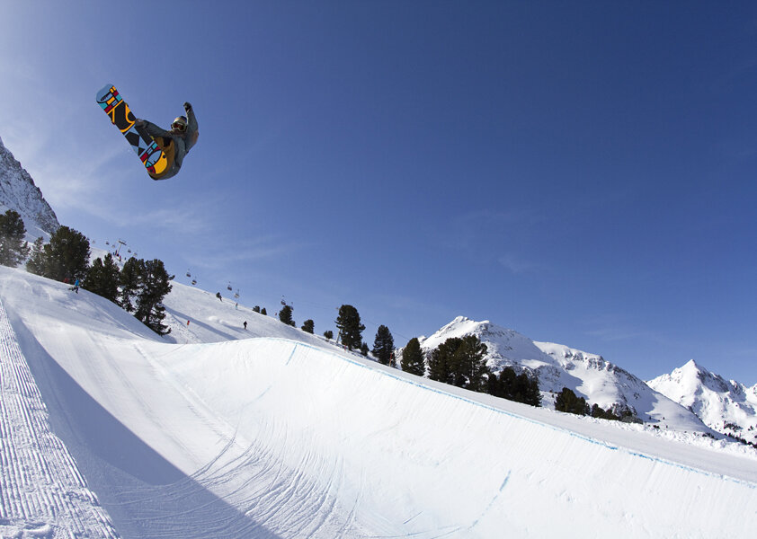 A snowboarder jumps high over the edge of a halfpipe in Kühtai.